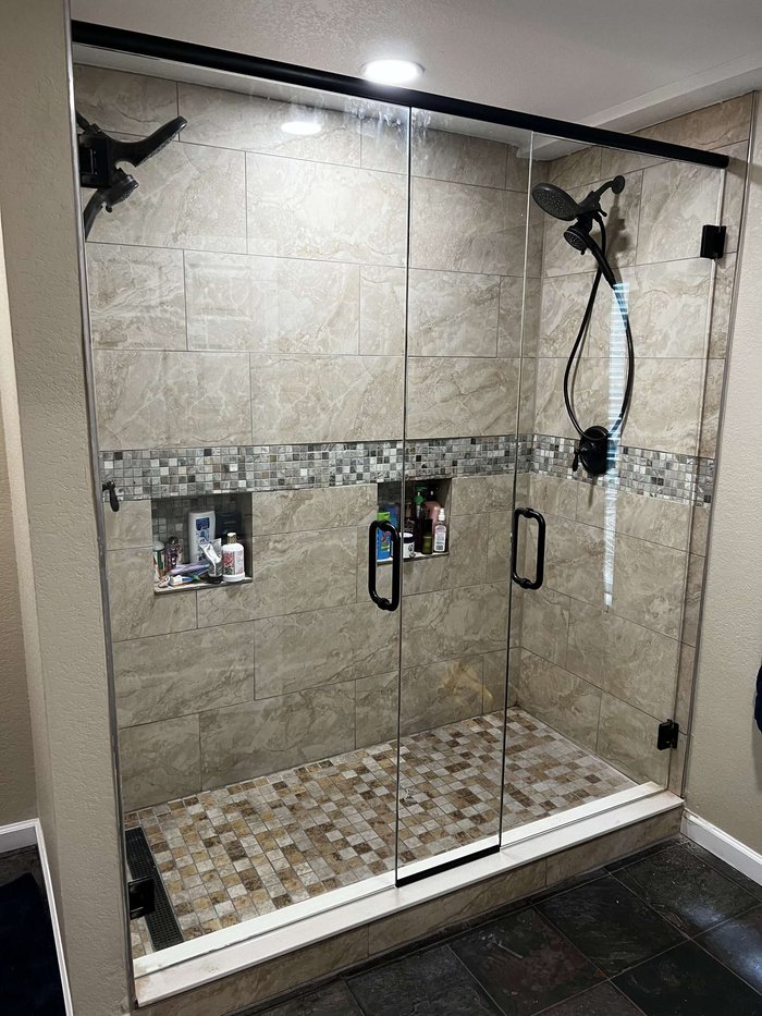 Frameless double swing-door shower with header, matte black hardware, and stone tile