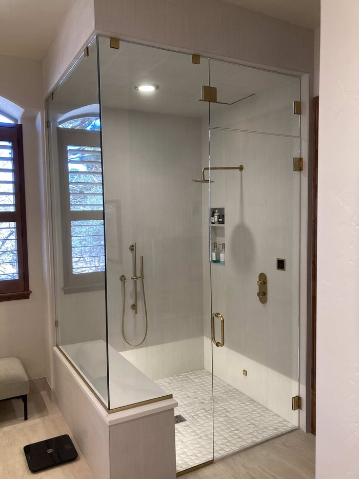 Frameless steam shower enclosure with satin brass gold hardware