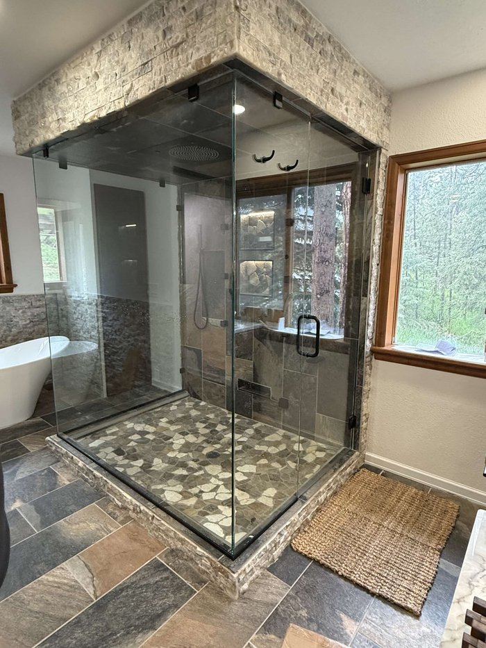 Frameless steam shower enclosure with stone surround and black hardware