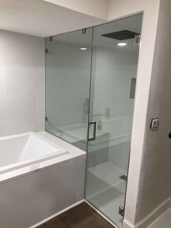 Frameless steam shower with brushed nickel clips beside a soaking tub