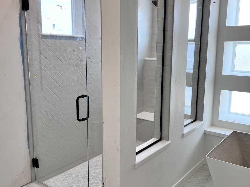 Frameless swing-door shower with window panels, matte black hardware, and herringbone tile
