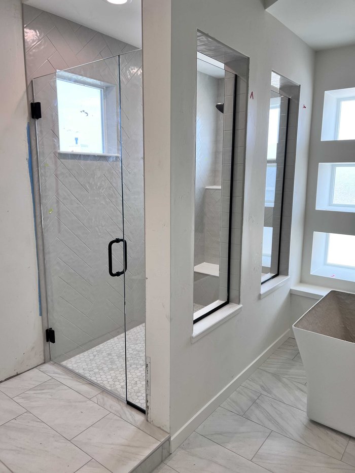 Frameless swing-door shower with window panels, matte black hardware, and herringbone tile