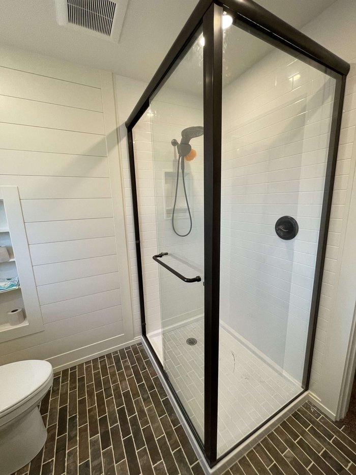 Semi-frameless bypass shower with matte black hardware and shiplap return panel
