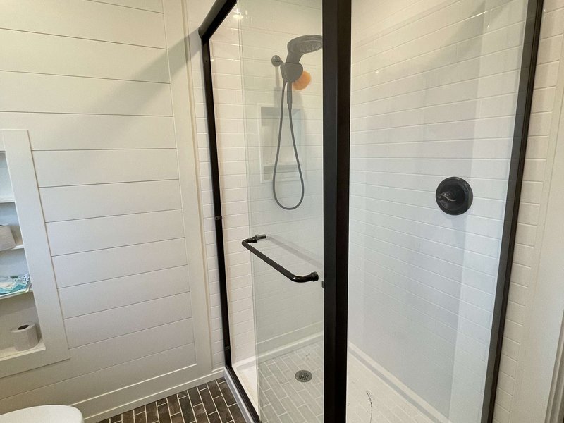 Semi-frameless bypass shower with matte black hardware and shiplap return panel