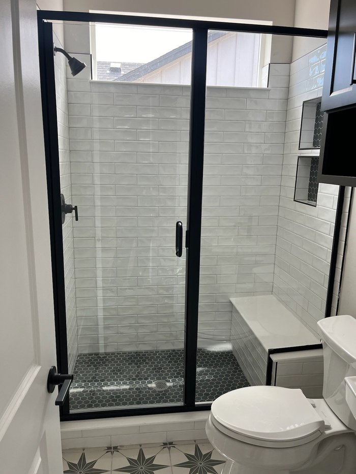 Semi-frameless swing-door shower with matte black hardware, subway tile walls, and hex tile floor